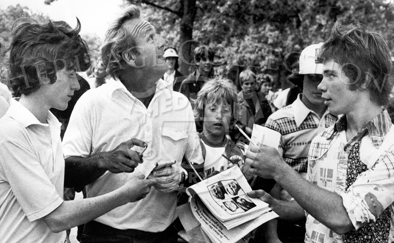 Surrounded by young autograph seekers, Arnold Palmer glances up at sound of a jet flying past as he heads for golf course at Medinah Country Club near Chicago suburban Itasca, Ill. Palmer and other golfers are practicing for this week's U.S. Open tournament.