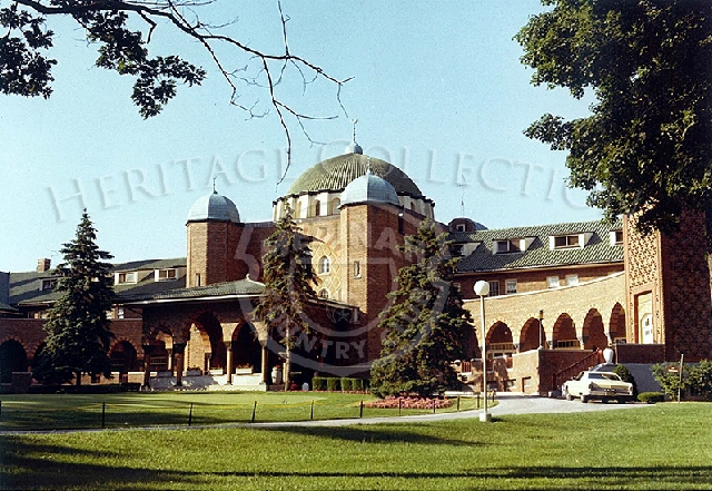 Color image of the front view of clubhouse in the 1970s, with a parked Oldsmobile in the scene.