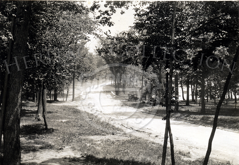 A black & white photograph shows the winding road through the grounds and around Lake Kadijah at Medinah Country Club. The road leads to the gun club. This image appears in August 1924 issue of The Red Fez.